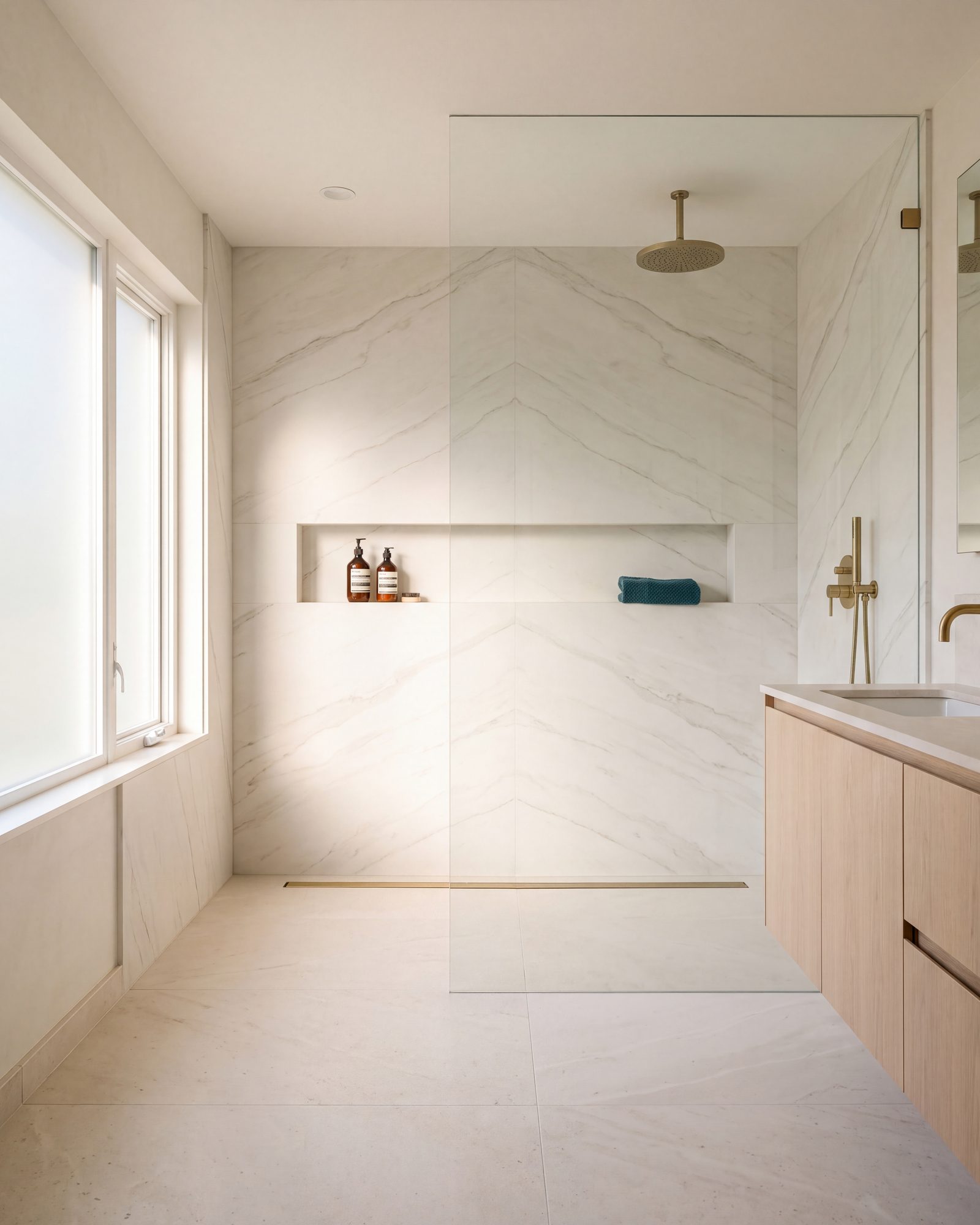 Curbless walk-in shower lined in book-matched porcelain slabs, with a linear drain, a ceiling rain head, a recessed niche and one fixed glass panel